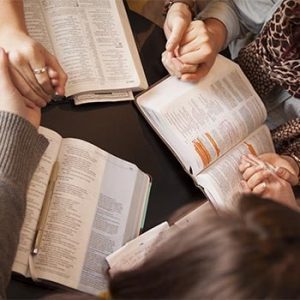 A group of young women bow their heads and pray with bibles.